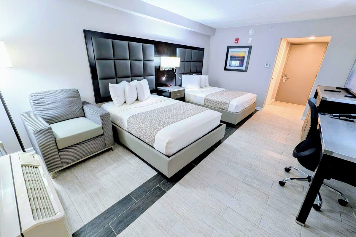A hotel room with a large bed, two bedside tables, a chair, a desk, and a computer.