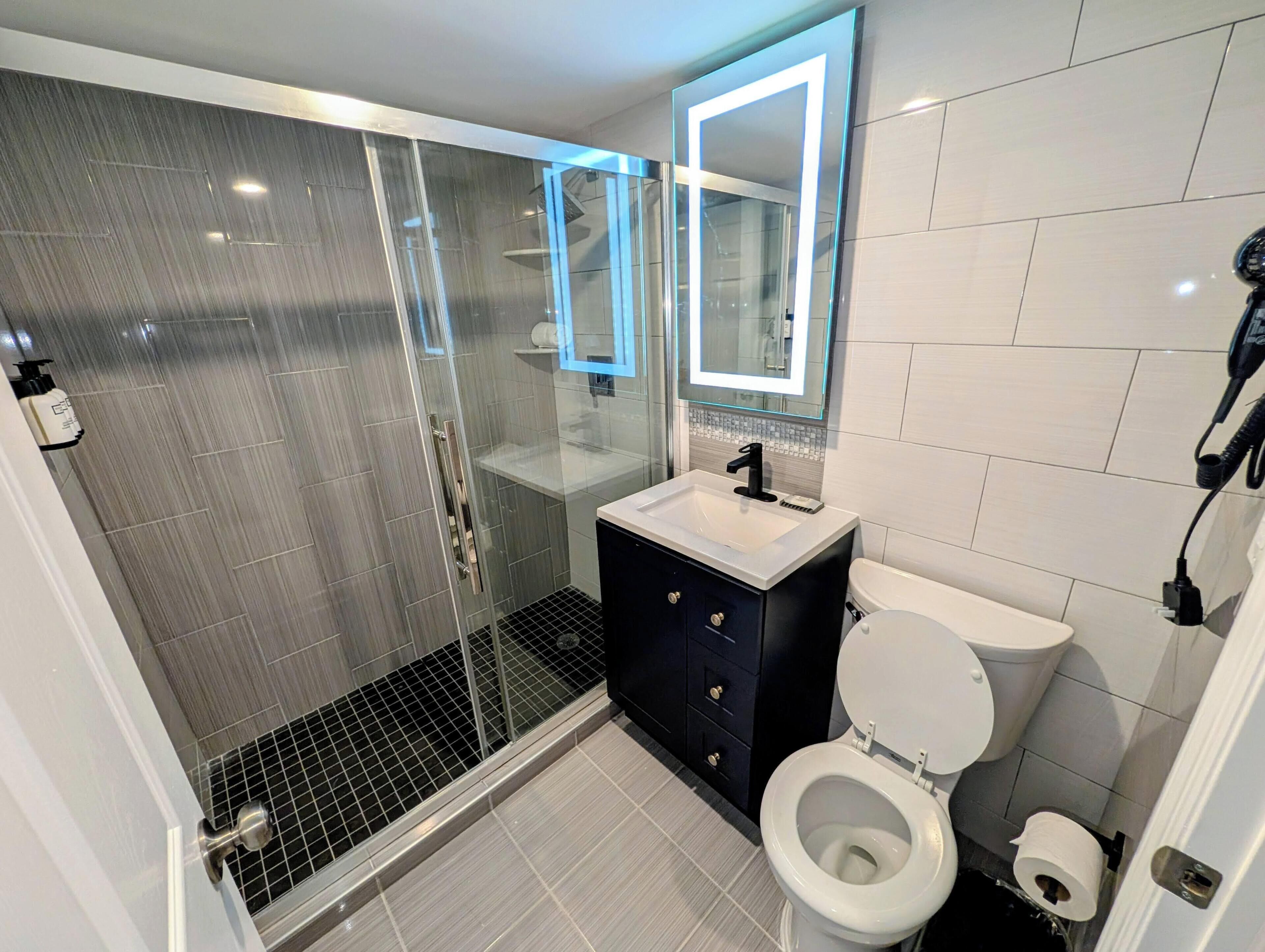 A modern bathroom with a glass-enclosed shower, a white sink, a black vanity, and a toilet.