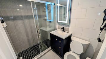 Een moderne badkamer met een douchecabine van glas, een witte wastafel, een zwart badkamermeubel en een toilet.