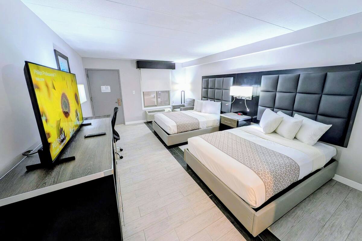A hotel room with a desk, two beds, a TV, and a nightstand.