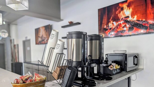 A coffee station with a coffee machine, paper cups, and a bowl of snacks. - SOHO Suites Atlantic City Beach Block (Atlantic City)