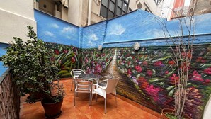 Um pátio com um mural, plantas em vasos e uma mesa com cadeiras.