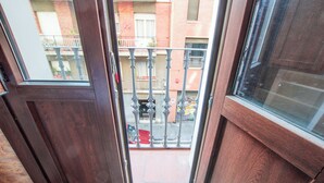 Vista de uma varanda com porta e janela de madeira, com vista para uma rua com um carro vermelho e um prédio com varanda.