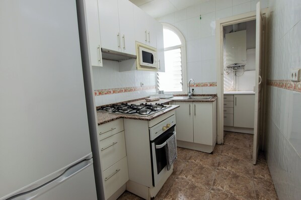 A compact kitchen with white cabinets, a gas stove, a microwave, and a sink. - Classic Sagrada Familia (Barcelona)