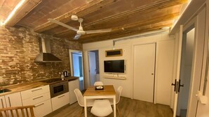 A compact kitchen with a wooden ceiling, a dining table with chairs, a bench, and a TV mounted on the wall. - Classic Palau Apartments (Barcelona)