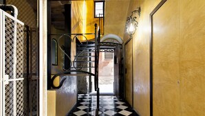 A hallway with a checkered floor, a metal spiral staircase, and a wooden door. - Classic Palau Apartments (Barcelona)