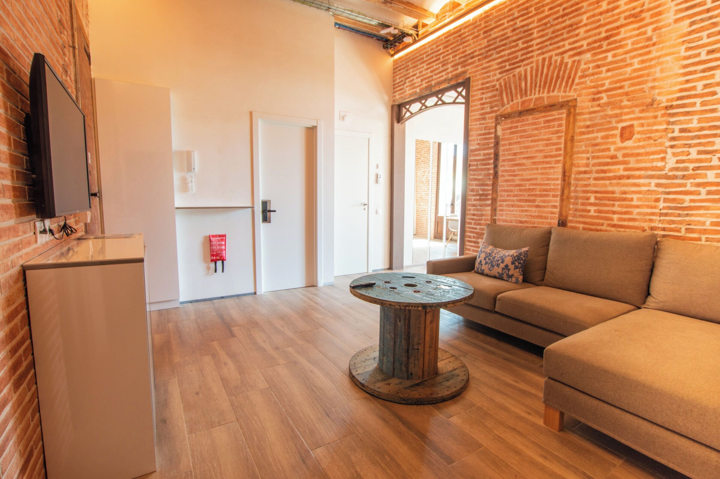 A modern living room with a brick wall, a round coffee table, a sofa, and a flat-screen TV mounted on the wall.