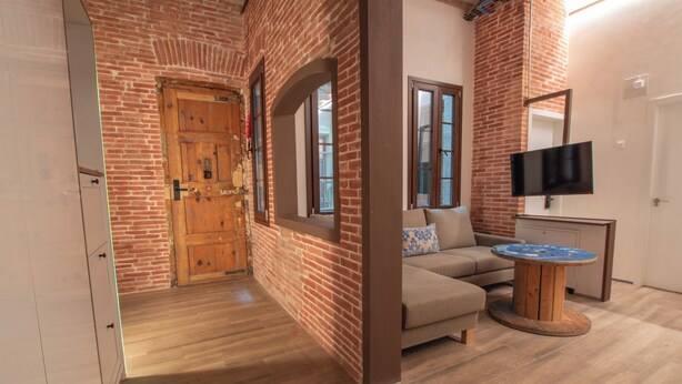 A room with a brick wall, wooden door, and a sofa with a round wooden table. - Classic Catedral Apartments  (Barcelona)