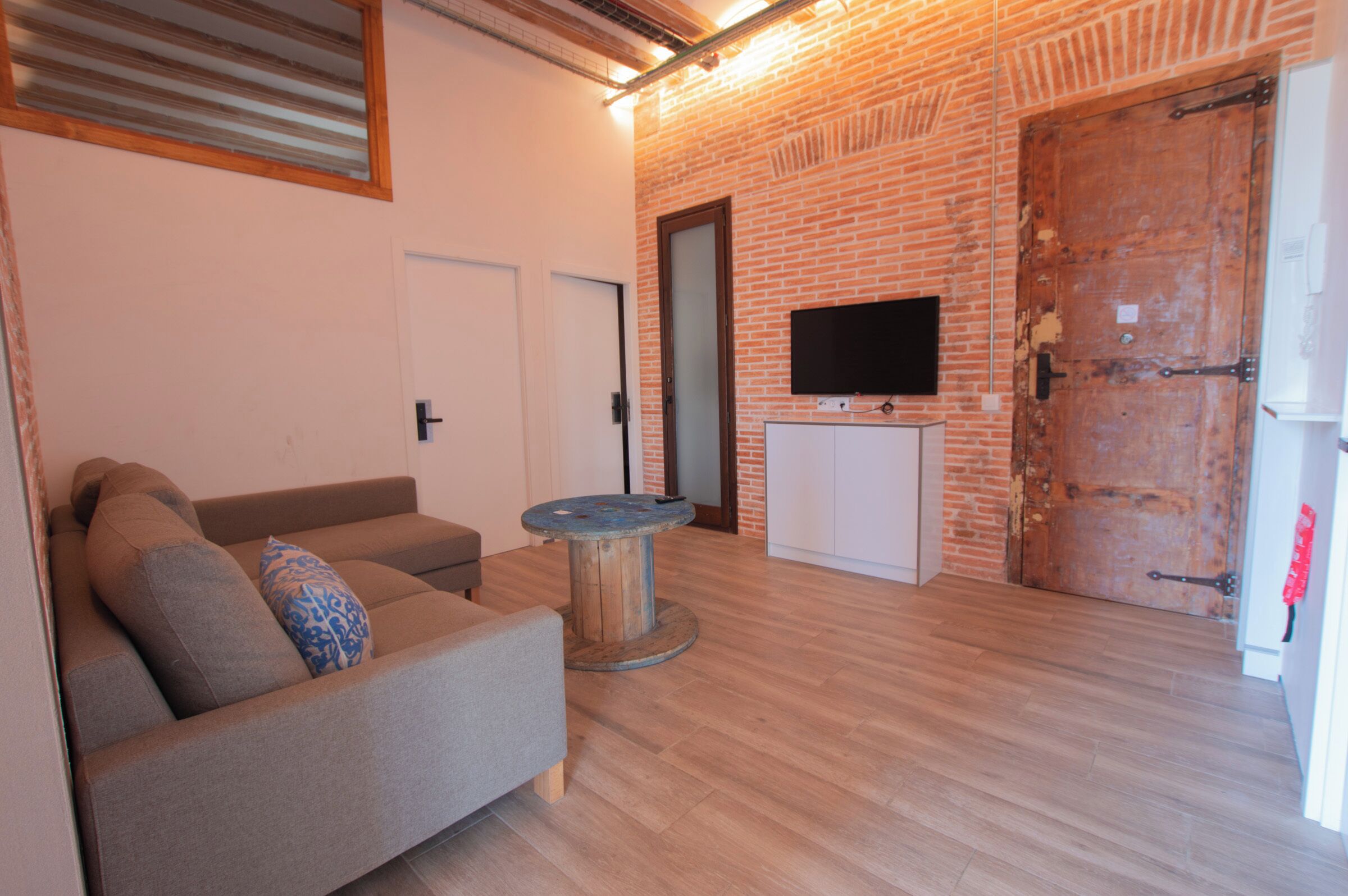 Uma sala de estar com parede de tijolos, um sofá, uma mesa redonda, uma televisão e uma porta.