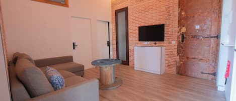 A living room with a brick wall, a sofa, a round table, a TV, and a door.
