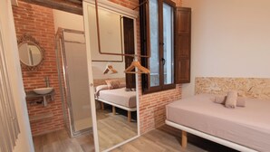 A bedroom with a bed, a mirror, a hanging light, and a bathroom with a sink and shower. - Classic Catedral Apartments  (Barcelona)
