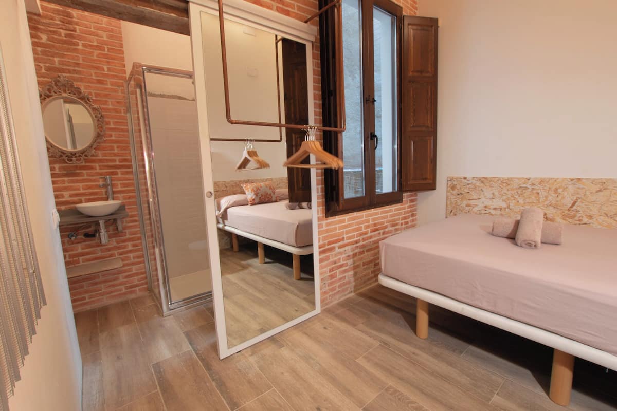 Ein Schlafzimmer mit Bett, Spiegel, Hängelampe und einem Badezimmer mit Waschbecken und Dusche.