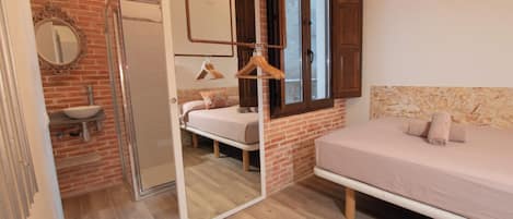 A bedroom with a bed, a mirror, a hanging light, and a bathroom with a sink and shower.