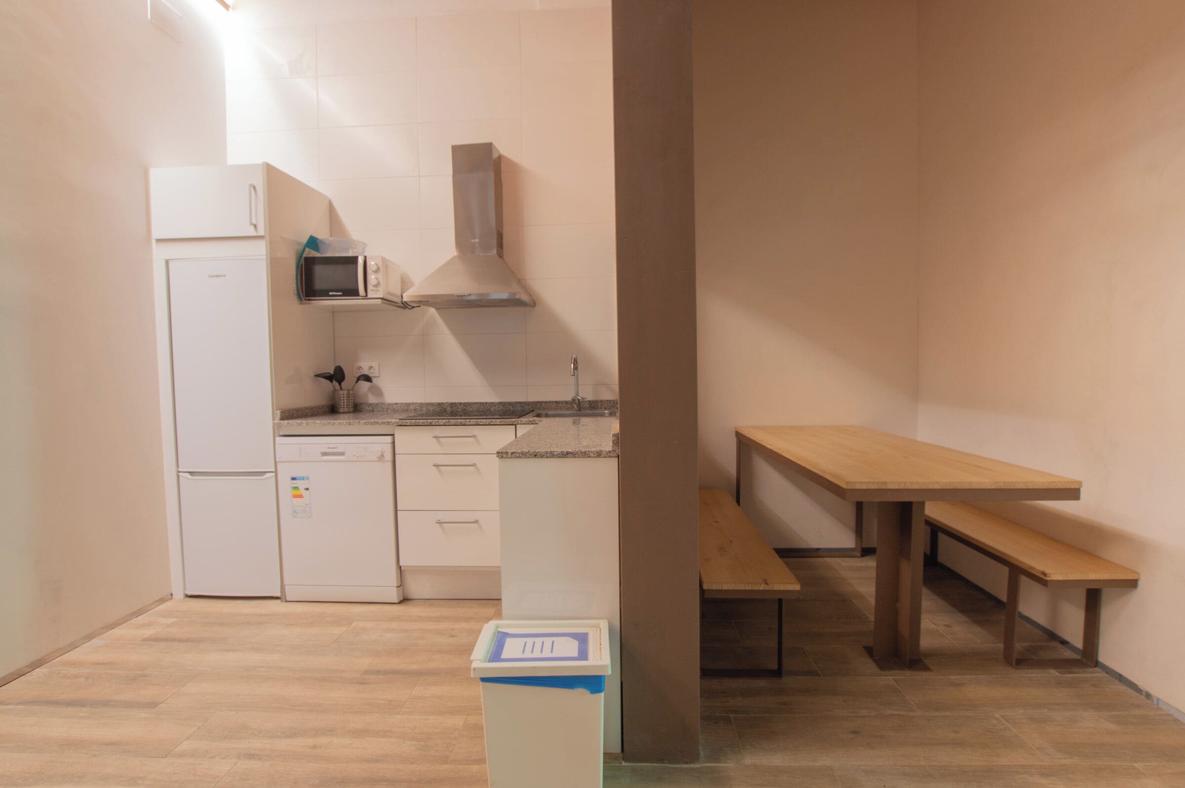 A compact kitchen with a refrigerator, microwave, and stove, and a wooden bench in the corner.