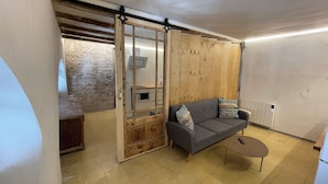 A modern living room with a sliding glass door leading to a kitchen, a grey sofa with patterned cushions, and a small round table. - Barcelona Classic Ramblas - Plaza Real (Barcelona)