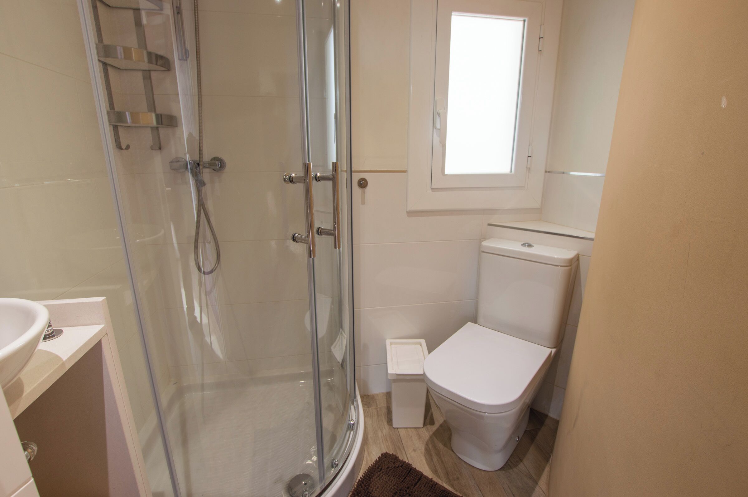 A bathroom with a glass-enclosed shower, a white toilet, and a small window above the toilet.