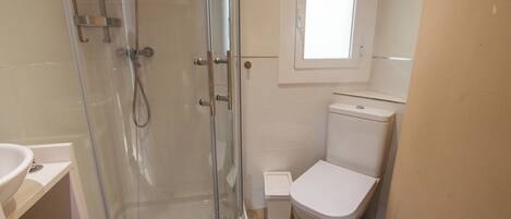 A bathroom with a glass-enclosed shower, a white toilet, and a small window above the toilet.