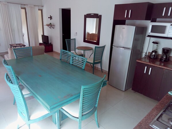 A dining area with a turquoise table and chairs, a refrigerator, a microwave, and a small kitchen counter with a blender. - Wonderful 2 bedroom family apartment in Tulum Centro Huanal (Tulum)