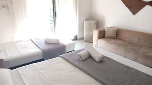 Hotellihuone, jossa on kaksi sänkyä, sohva, seinälle kiinnitetty koriste-esine ja ikkuna, jossa on verhot.