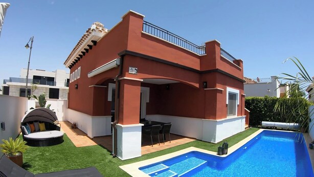 A modern house with a swimming pool, a covered patio, and a garden area with artificial grass and outdoor furniture.