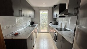 A modern kitchen with dark cabinets, stainless steel appliances, and a view through a glass door to the outdoors.