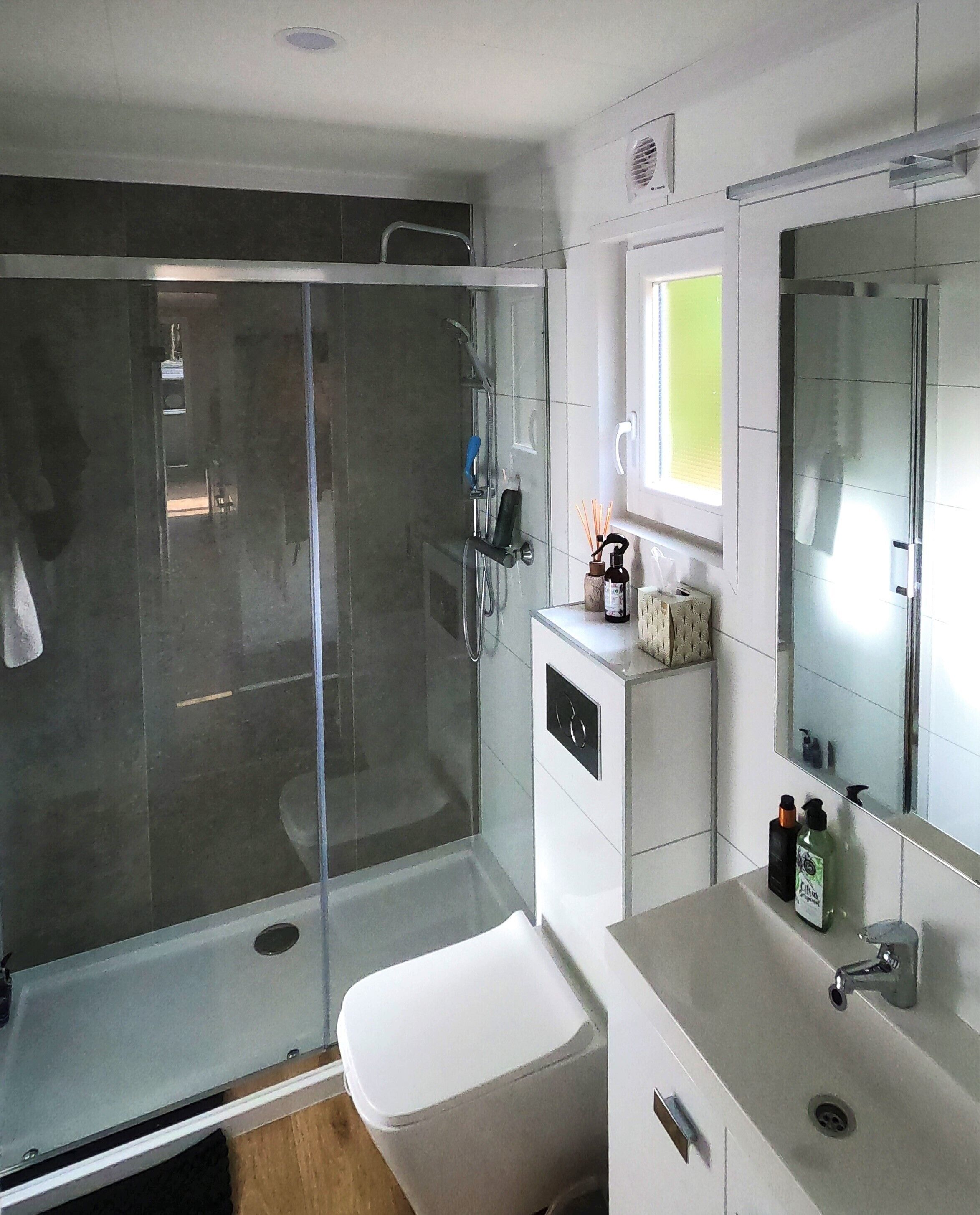 A modern bathroom with a glass shower enclosure, a white sink, and a mirror above the vanity.