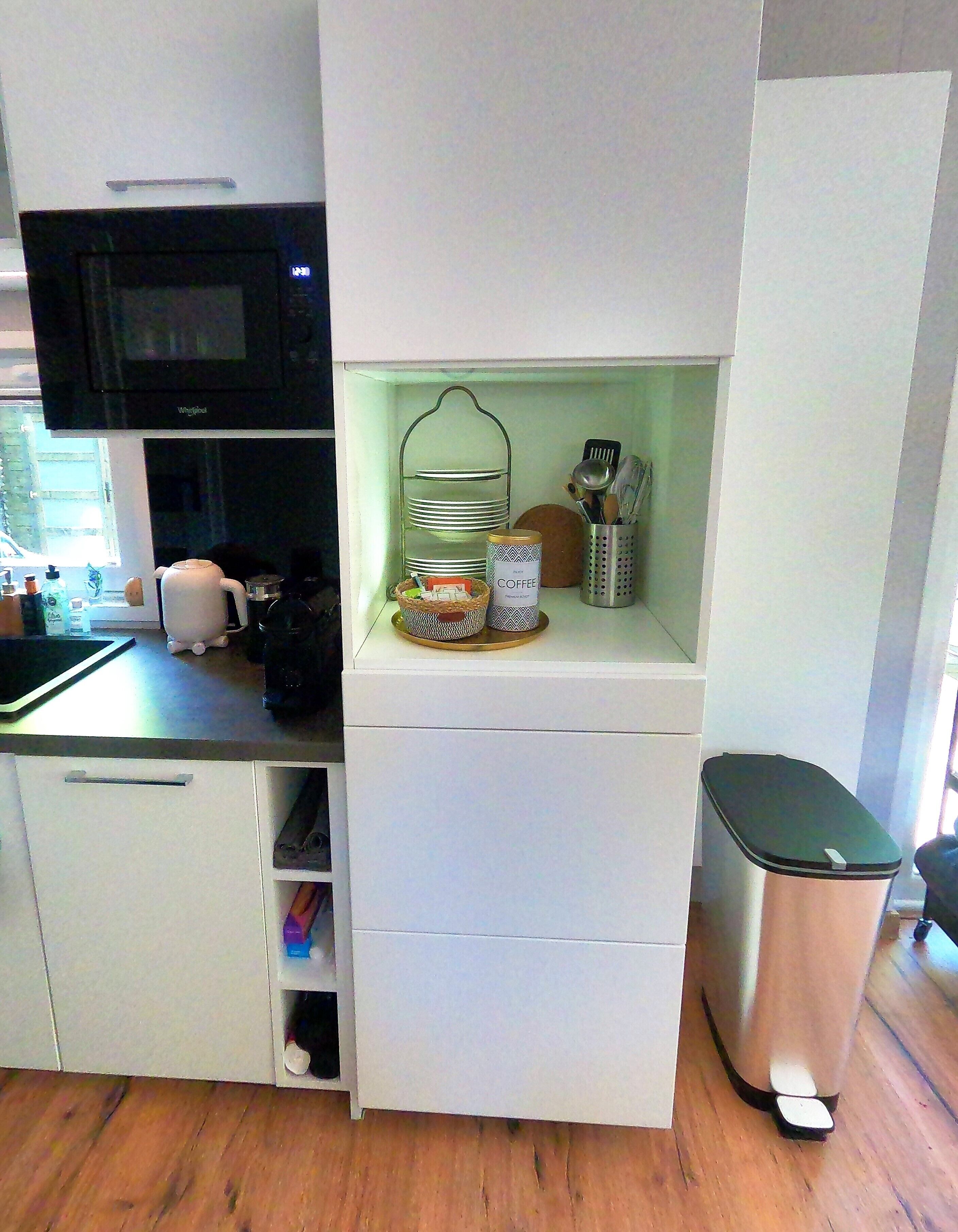 A compact kitchen with a microwave, a coffee station, and a trash bin.