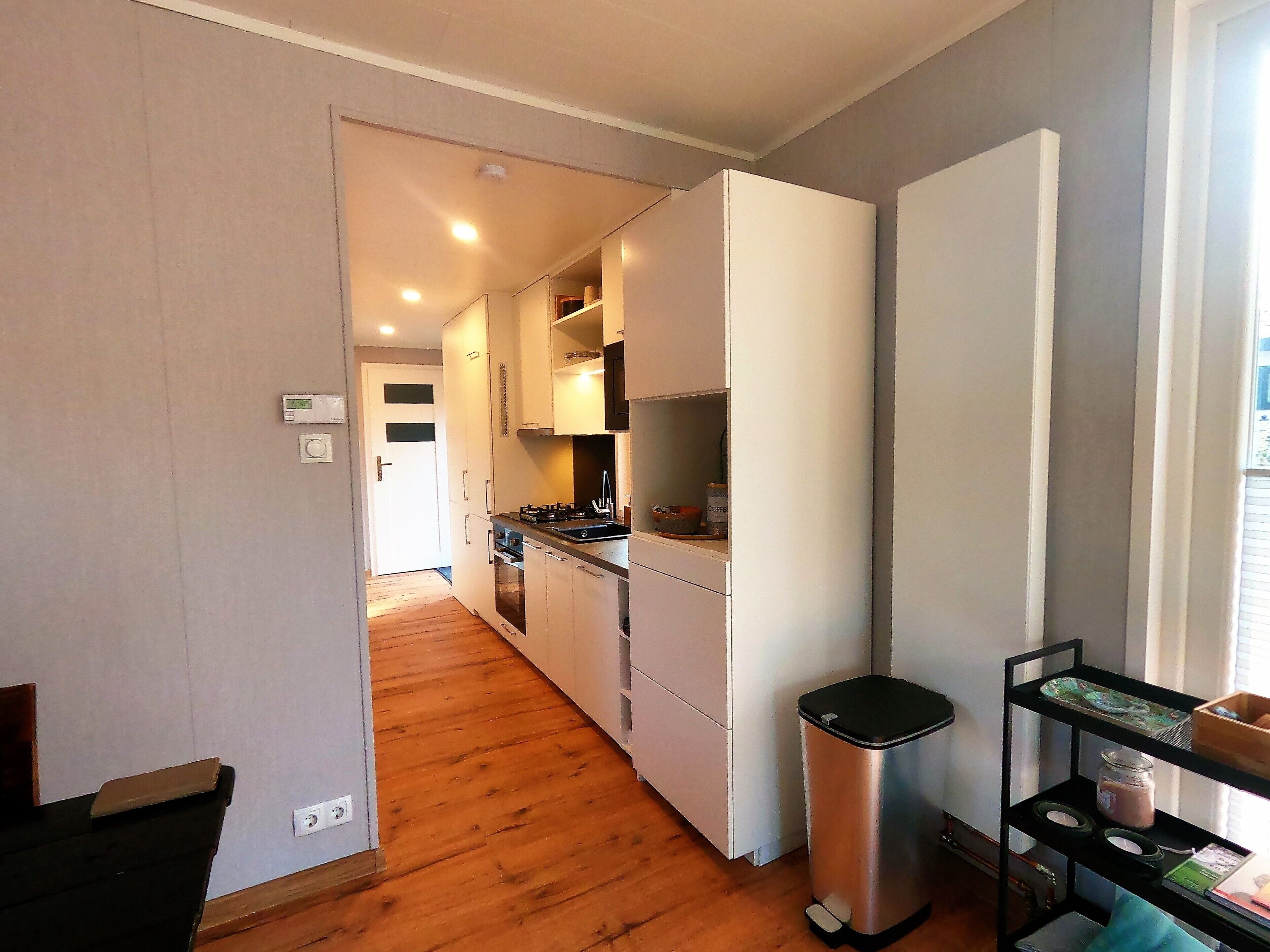A compact kitchen with white cabinets, a stainless steel trash bin, and a small shelf with jars.