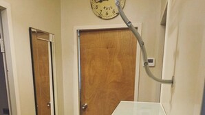 Un corridoio stretto con una porta in legno, un piccolo gradino e un bancone bianco. Un orologio è fissato alla parete.