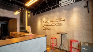 Eine moderne Bar mit einer Neonreklame, einer Theke und zwei roten Barhocker.