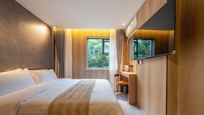 Ein modernes Hotelzimmer mit einem großen Bett, einem Schreibtisch mit Stuhl, einem an der Wand montierten Fernseher und einem Fenster mit Blick auf Grünflächen.