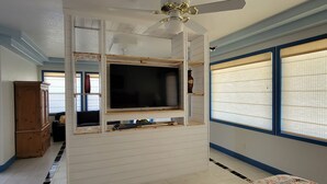 A bedroom with a large bed, a TV mounted on a white wall, a ceiling fan, and a window with blinds. - Beautiful Riverside Home (T or C)