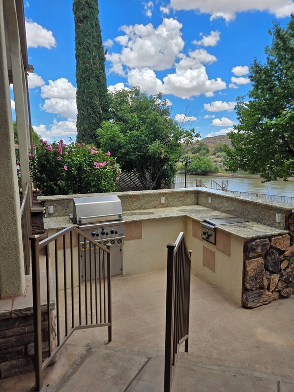 An outdoor kitchen area with a grill, a stone wall, and a view of a river. - Beautiful Riverside Home (T or C)