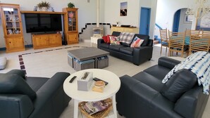 A spacious living room with a large flat-screen TV, comfortable seating, a fireplace, and a ceiling fan. - Beautiful Riverside Home (T or C)