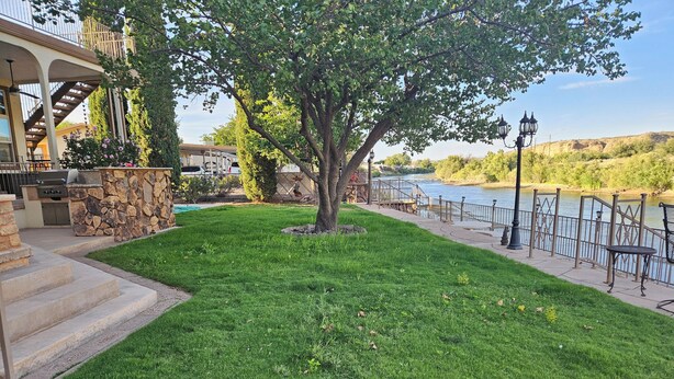 A well-maintained lawn with a stone barbecue area, a wooden deck, and a view of a river. - Beautiful Riverside Home (T or C)