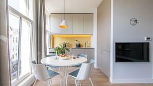 A modern kitchen with white cabinets, a dining table with four chairs, a plant, and a TV mounted on the wall. - City Apartment Darling (Rotterdam)