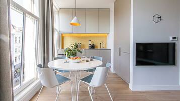 Una cocina moderna con armarios blancos, una mesa de comedor con cuatro sillas, una planta y un televisor montado en la pared.