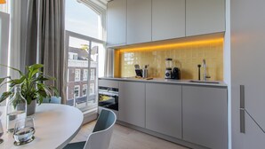 A modern kitchen with white cabinets, a built-in oven, a coffee machine, and a window with curtains. - City Apartment Darling (Rotterdam)