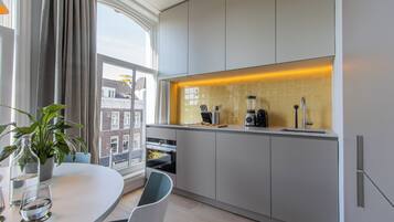 A modern kitchen with white cabinets, a built-in oven, a coffee machine, and a window with curtains.
