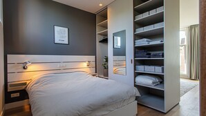 A modern bedroom with a large bed, built-in shelving, a bedside table, and a wall-mounted mirror. - City Apartment Darling (Rotterdam)