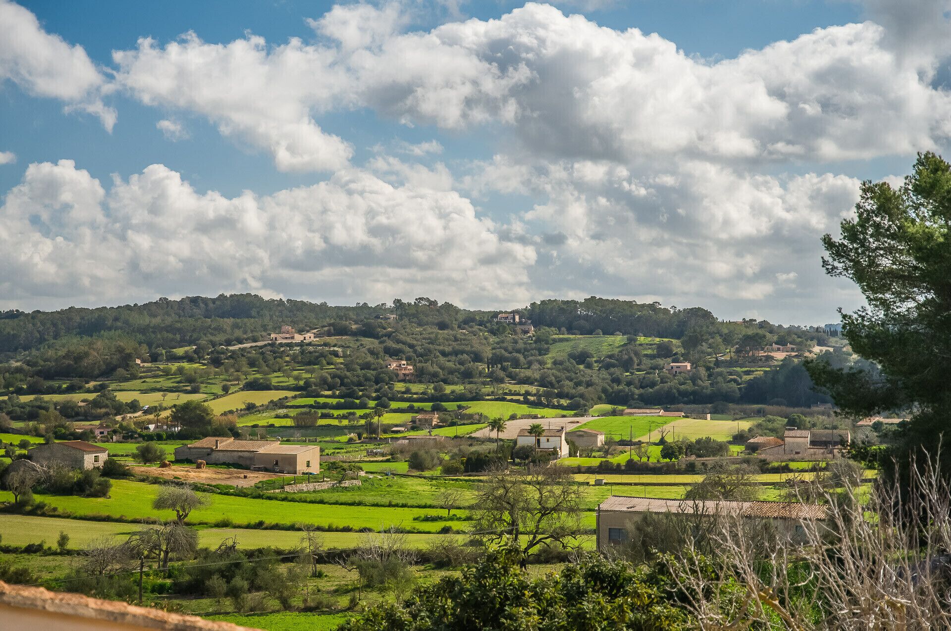 A rural landscape with rolling hills, scattered houses, and a clear sky.
