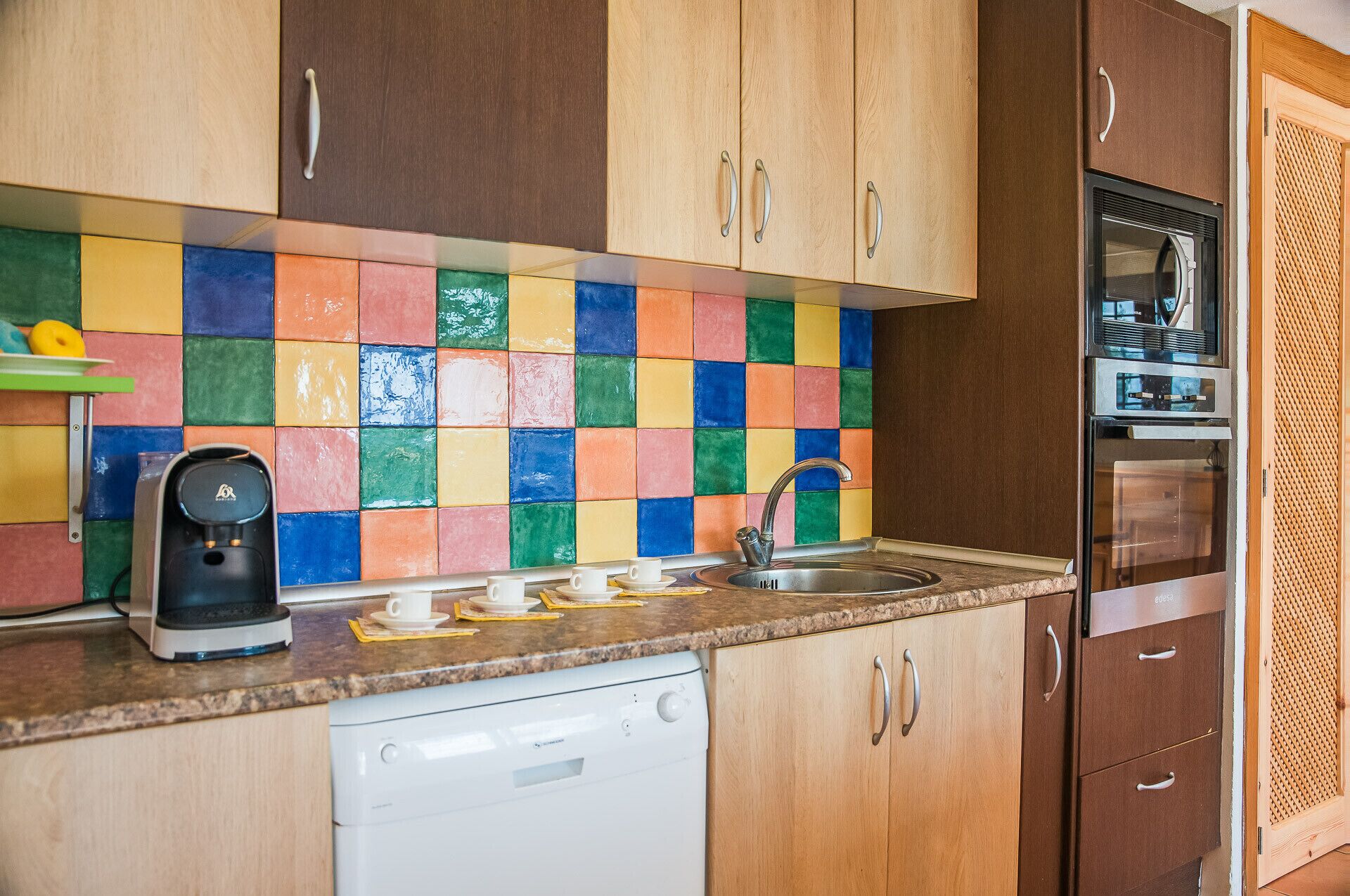 A kitchen with wooden cabinets, a colorful tiled backsplash, a coffee maker, a sink, and a dishwasher.