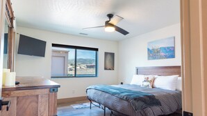 A bedroom with a bed, a ceiling fan, a window with a view, and a wooden dresser. - Cozy Dark Sky Retreat Near Sedona • Hot Tub, Sauna & Views (Cornville)