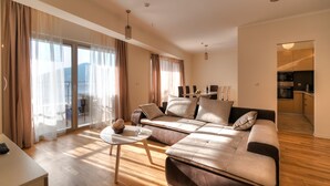 A modern living room with a sofa, a coffee table, and a view of the city through large windows. - Sea View Apartments MonteBook (Becici)