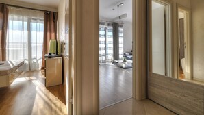 A modern hotel room with a wooden floor, a bed, a desk, and a view of the balcony. - Sea View Apartments MonteBook (Becici)