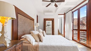 Ein Schlafzimmer mit einem großen Bett, einer Holzkommode, einem Deckenventilator und Blick ins Freie durch eine Glastür.