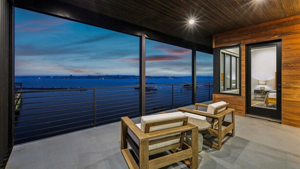 A balcony with a view of the water, wooden furniture, and a modern interior design. - PK Juniper Overlook | Brand new home! | Sleeps 17 w 2 living rooms, kayaks/games (Graford)