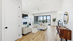 A spacious living room with a fireplace, large windows, and a view of the city. - PK Juniper Overlook | Brand new home! | Sleeps 17 w 2 living rooms, kayaks/games (Graford)