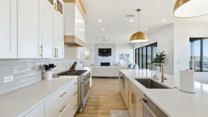 A modern kitchen with white cabinetry, a central island, and a large window providing natural light. - PK Juniper Overlook | Brand new home! | Sleeps 17 w 2 living rooms, kayaks/games (Graford)