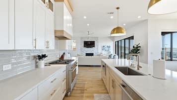 Une cuisine moderne avec des meubles blancs, un îlot central et une grande fenêtre qui laisse entrer la lumière naturelle.